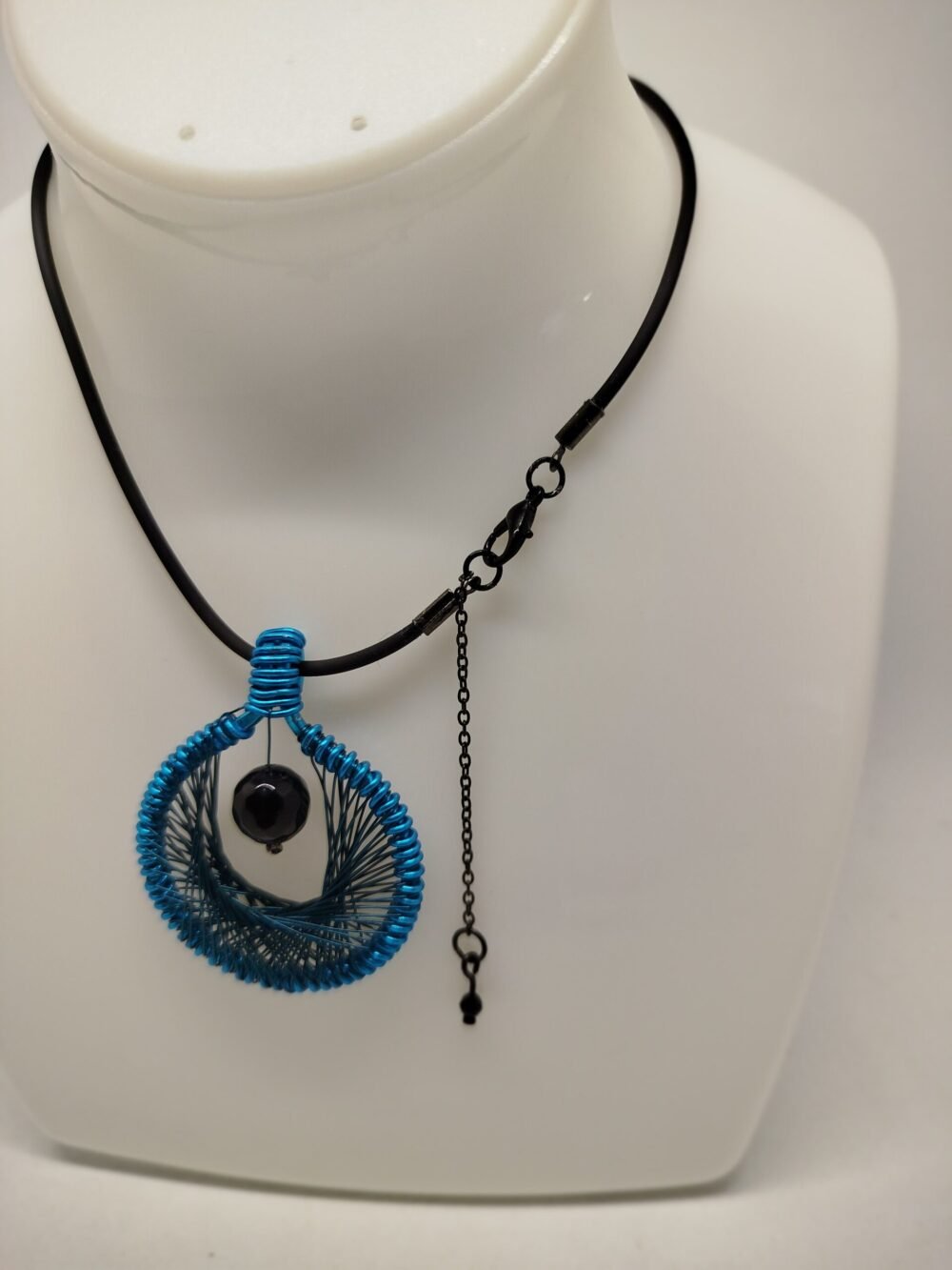 Le pendentif de 4 cm créé en fil aluminium turquoise et tissé à l'intérieur. Une belle pierre Onyx à facettes est fixé au centre.Le collier de 45 cm de longueur est en caoutchouc avec fermoir mousqueton.