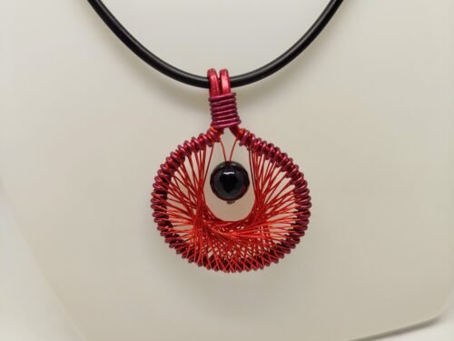 Le pendentif de 4 cm créé en fil aluminium rouge et tissé à l'intérieur. Une belle pierre Onyx à facettes est fixé au centre.Le collier de 45 cm de longueur est en caoutchouc avec fermoir mousqueton.