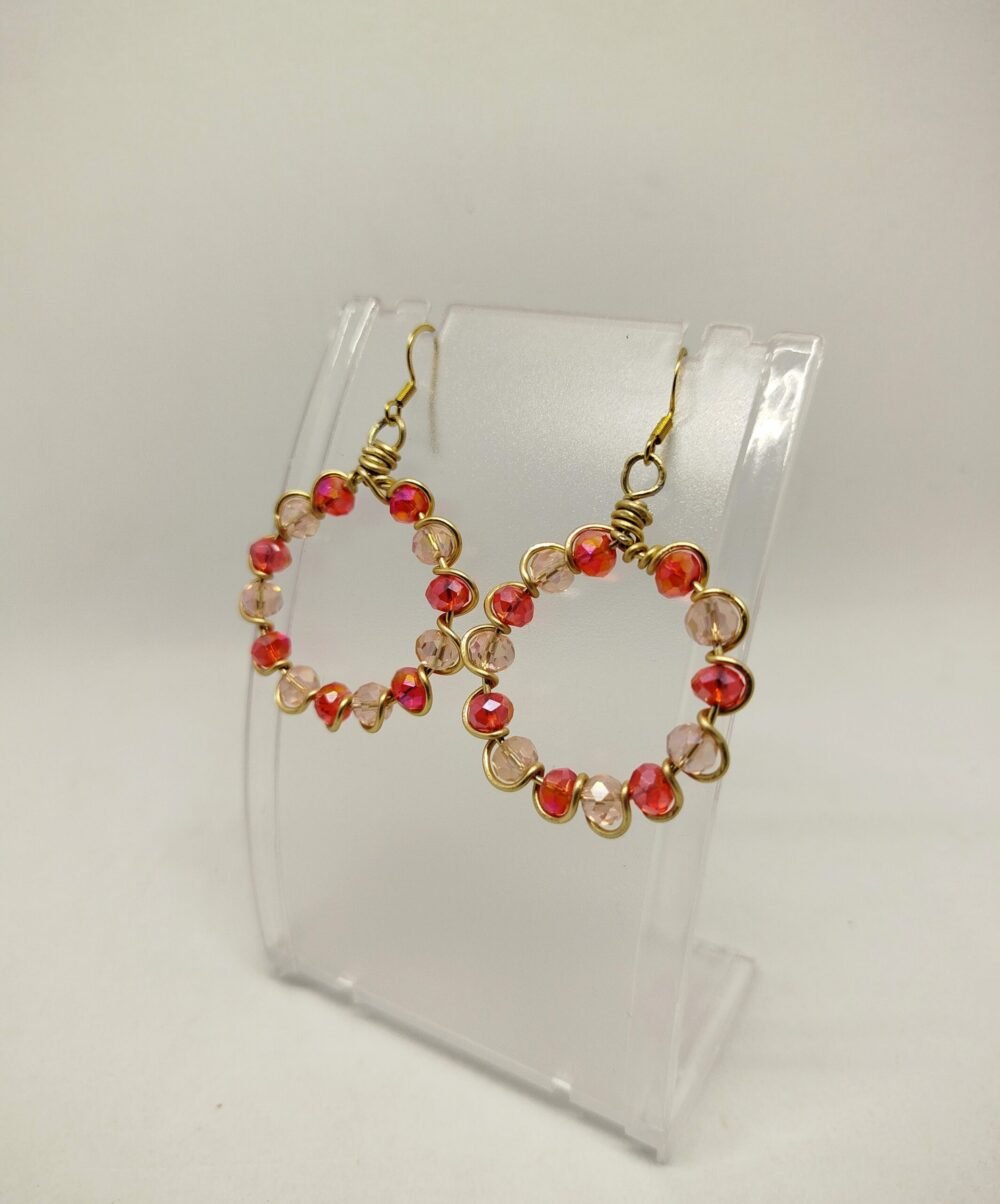 créoles façonnées avec des perles en verre à facettes rouge, entourées avec du fil aluminium doré. Leur diamètre est de 3 cm. Les crochets sont de couleur dorée et en acier chirurgical et hypoallergénique