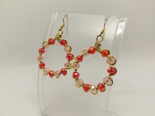 créoles façonnées avec des perles en verre à facettes rouge, entourées avec du fil aluminium doré. Leur diamètre est de 3 cm. Les crochets sont de couleur dorée et en acier chirurgical et hypoallergénique