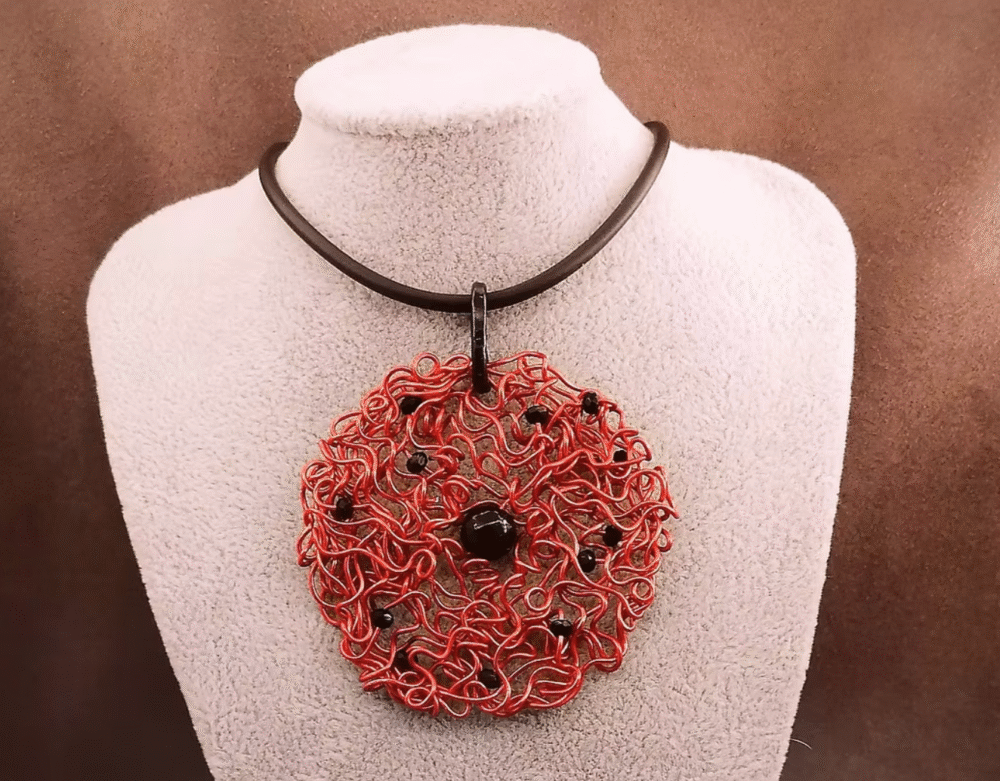 Le pendentif de 6,5 cm façonné à la main en fil d’aluminium rouge, et des perles à facettes noires, une pierre naturelle Onyx au centre