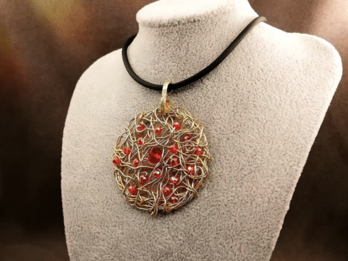 Le pendentif de 5cm confectionné à la main avec du fil aluminium doré et des petites perles à facettes rouges fixé sur un collier en caoutchouc noir d’une longueur de 50 cm avec fermoir mousqueton couleur doré. Le pendentif de 5cm confectionné à la main avec du fil aluminium doré et des petites perles à facettes rouges fixé sur un collier en caoutchouc noir d'une longueur de 50 cm avec fermoir mousqueton couleur doré.