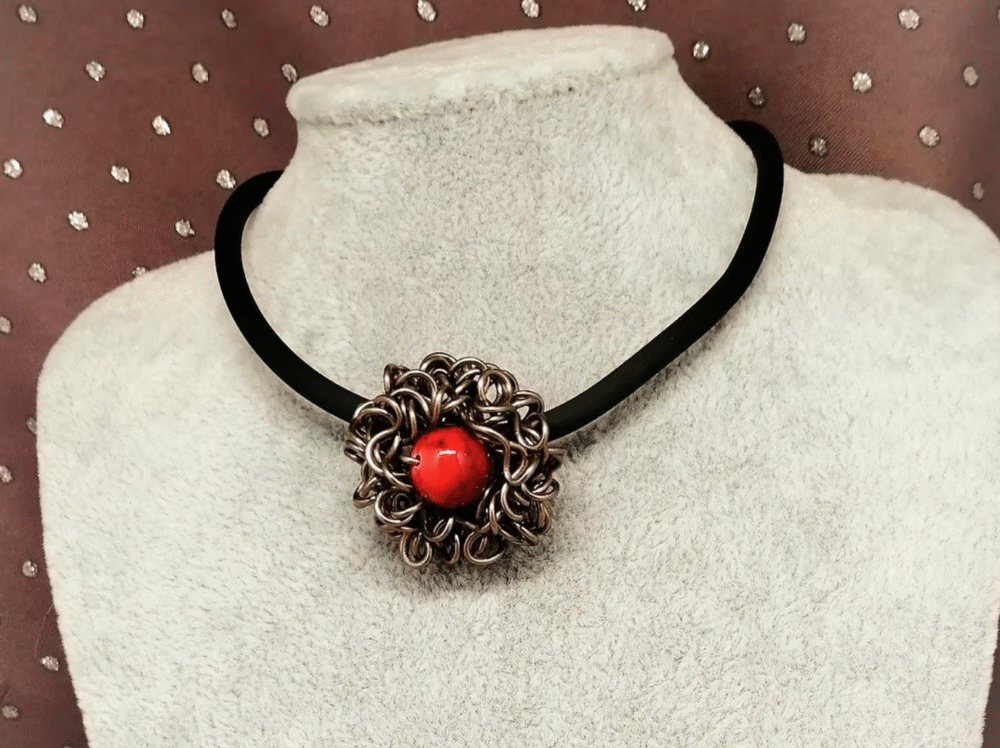 magnifique pendentif en fil aluminium marron entoure une belle pierre naturelle Howlite Rouge fixé sur un collier en caoutchouc noir avec fermoir mousqueton. Il se porte ras du cou. La longueur est de 40 cm.