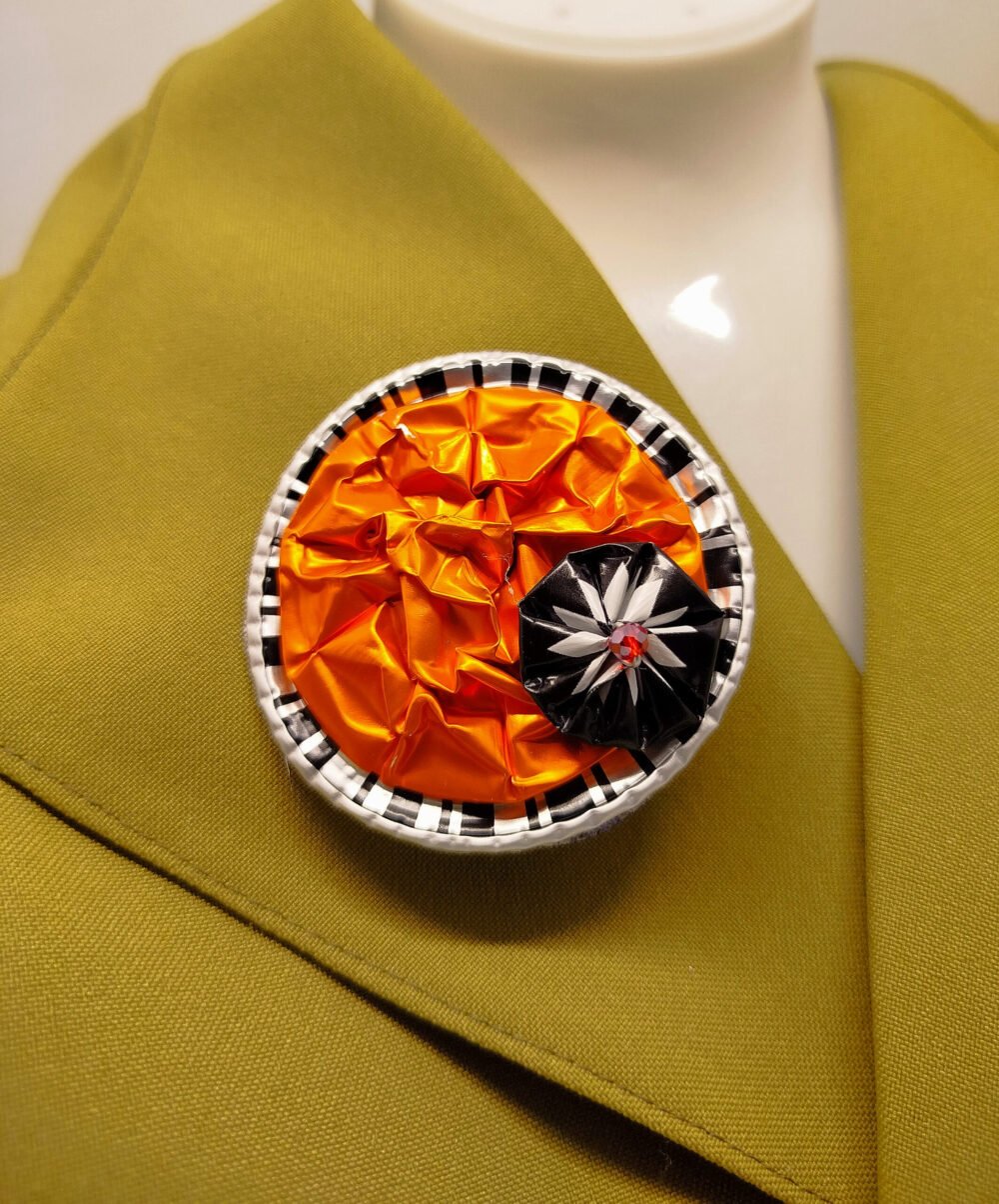 broche créé en capsules de café orange avec petite fleur noir fixé dessus diamètre 6 cm éco-créative